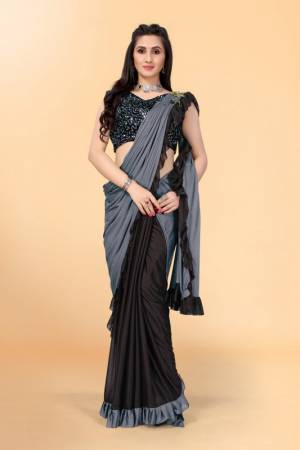 Get glowing in this pretty ready-to-wear lycra saree. The colorblocked saree is made of lycra fabric in black and grey color with ruffles detailing on hem beautified by brooch on shoulder making it more attractive. This saree comes along with unstitched velvet diamond embellished fabric blouse piece. It is perfect for parties, family functions when paired with beautiful jewellery and pair of heels to complete the look.