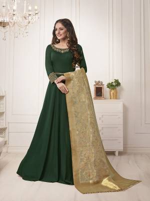 Bright And Visually Appealing Color Is Here With This Designer Floor Length Suit In Dark Green Color Paired With Beige Colored Dupatta. Its Top Is Fabricated On Muslin Silk Paired With Santoon Bottom And Banarasi Silk Dupatta. Buy This Now.