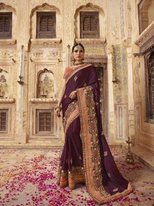 Catch All The Linelight Draping This Designer Saree In Wine Color Paired With Contrasting Dark Peach Colored Blouse. This Saree And Blouse are Silk Based Beautified With Heavy Embroidery. 