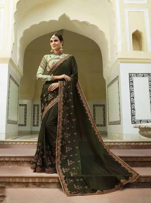 Get Ready For The Upcoming Wedding Season With This Designer Saree In Dark Olive Green Color Paired With Pastel Green Colored Blouse. This Saree And Blouse Are Silk based With A Touch Of Tissue In Blouse. Carry Minimal Accessories With This Pretty Heavy Saree. 