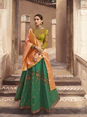 Shades In Green Are Here With This Heavy Designer Lehenga Choli In Pear Green Colored Blouse Paired With Dark Green Colored Lehenga And Contrasting Orange Colored Dupatta. This Lehenga Choli Is Silk Based Paired With Two Dupattas, One In Net And Another Is Fabricated On Banarasi Art Silk .