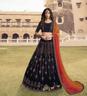 You Will Definitely Earn Lots Of Compliments Wearing This Heavy Designer Lehenga Choli In Navy Blue Color Paired With Contrasting Red And Orange Colored Dupatta. Its Blouse And Lehenga Are Fabricated On Velvet Paired With Net Fabricated Dupatta. All Its Fabrics Esnures Superb Comfort All Day Long. 