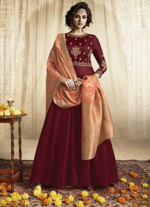 For A Royal Look, Grab This Designer Readymade Floor Length Gown In Maroon Color Paired With Contrasting Peach Colored Dupatta. Its Top Is Fabricated On Satin Linen Paired With Jacquard Silk Fabricated Dupatta. It Has Beautiful Embroidery Over The Yoke And Sleeves. Buy Now.