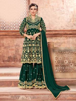 This Festive Season, Grab This Heavy Designer Sharara Suit In Dark Green Color Paired With Dark Green Colored Bottom And Dupatta. Its Heavy Embroidered Top And Bottom Are Fabricated On Satin Georgette Paired With Chinon Fabricated Dupatta. Buy This Semi-Stitched Suit Now.