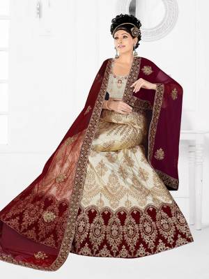 Flaunt Your Rich And Elegant Taste With Some Subtle Color Pallet In Your Bridal Wear. Grab This Heavy Designer Lehenga Choli In Cream Color Paired With Maroon Colored Dupatta. Its Blouse Are Lehenga are Satin Silk Based Paired With Net Fabricated Dupatta. 