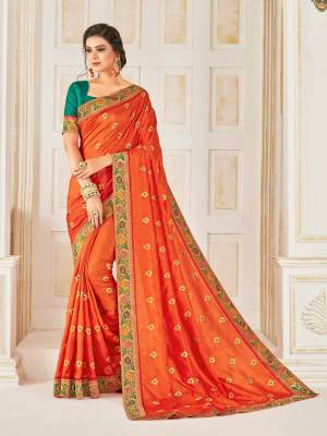 Celebrate This Festive Season Wearing This Designer Silk Based Saree In Orange Color Paired With Contrasting Teal Blue Colored Blouse. This Saree Is Beautified With Small Embroidered Buttis And Jacquard Lace Border. 