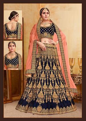 Get Ready For Your D-Day With This Heavy Designer Bridal Lehenga Choli In Navy Blue Color Paired With Contrasting Dark Peach Colored Dupatta. Its Heavy Embroidered Blouse And Lehenga Are Fabricated On Velvet Paired With Net Fabricated Dupatta. 