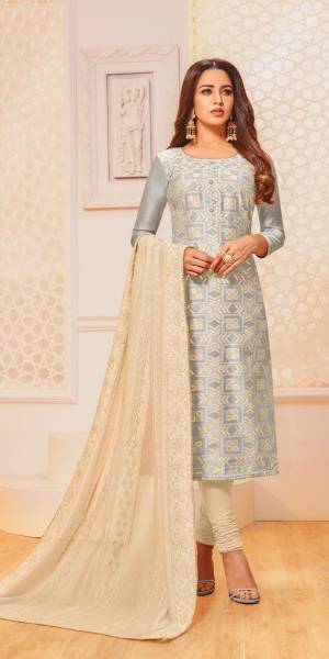 For Your Semi-Casual Wear, Grab This Pretty Semi-Stitched Suit In Light Grey Colored Top Paired With Cream Colored Bottom And Dupatta. Its Top Is Fabricated On Jacquard Silk Paired With Cotton Bottom And Chanderi Silk Dupatta. 